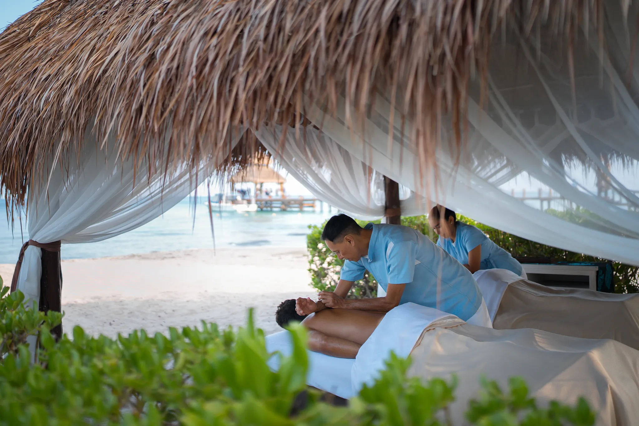 Couple enjoying a beachfront massage under a palapa at Secrets Aura Cozumel, surrounded by ocean views and tropical serenity.