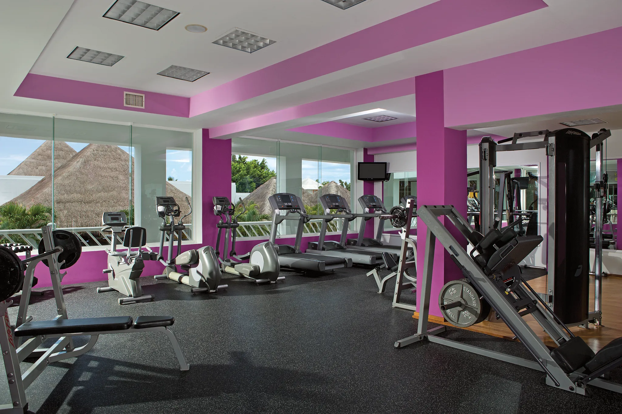 Modern fitness center with cardio and strength equipment at Secrets Aura Cozumel, featuring large windows and tropical views.