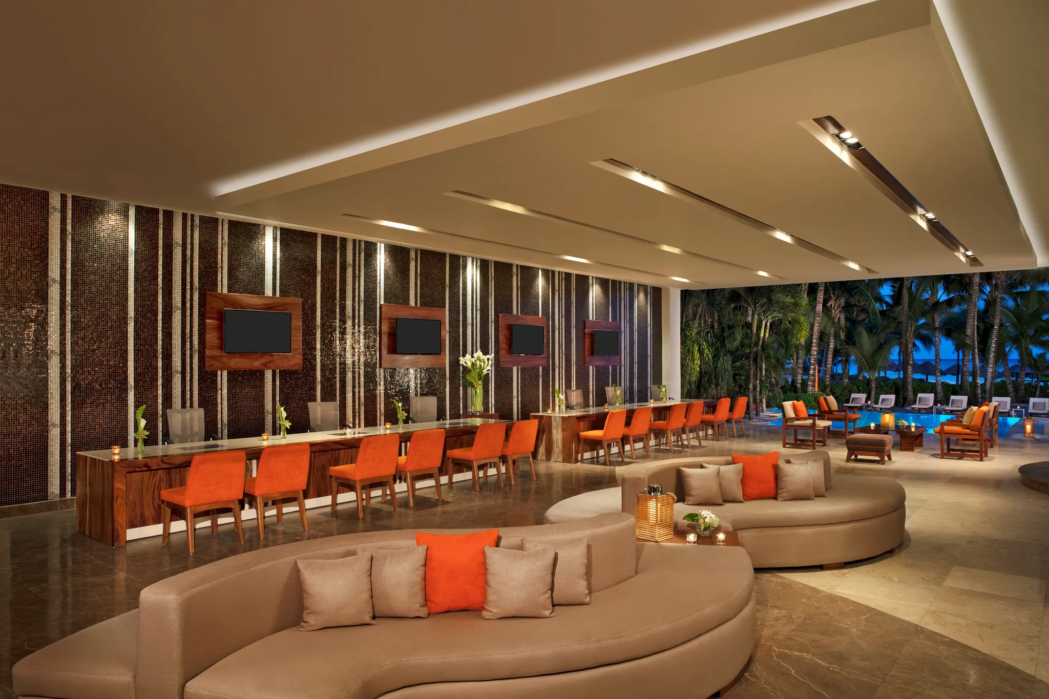 Stylish open-air lobby lounge with modern seating and warm lighting at Secrets Aura Cozumel overlooking tropical gardens.