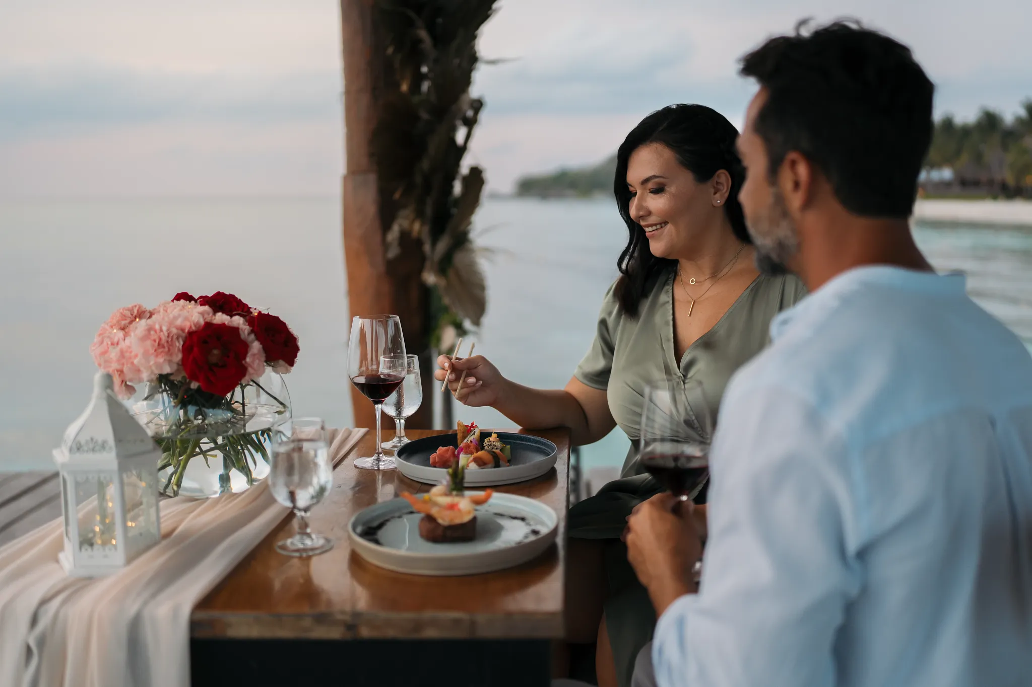 Couple enjoying a romantic oceanfront dinner with wine at sunset at Secrets Aura Cozumel.
