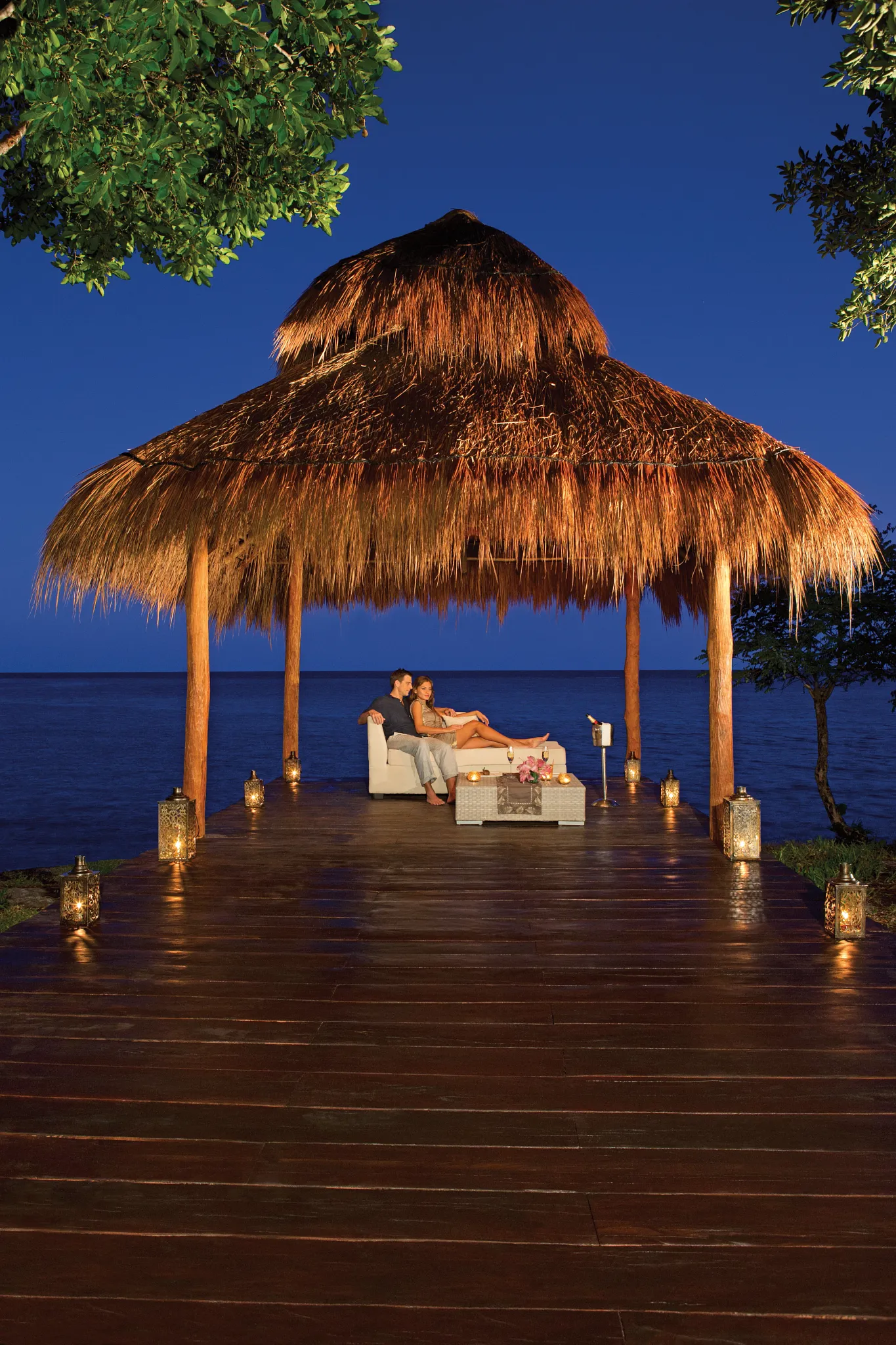 Romantic private dinner setup under a palapa by the ocean at Secrets Aura Cozumel at night.