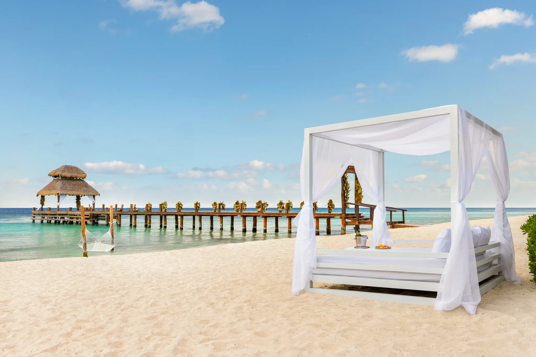 Private beach cabana with white drapes and oceanfront pier at Secrets Aura Cozumel in Cozumel, Mexico.