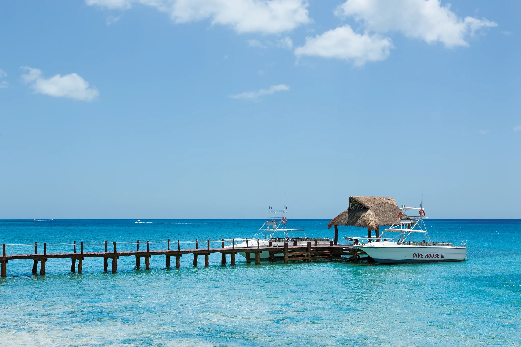 Dive boats docked at pier at Secrets Aura Cozumel over clear Caribbean water.