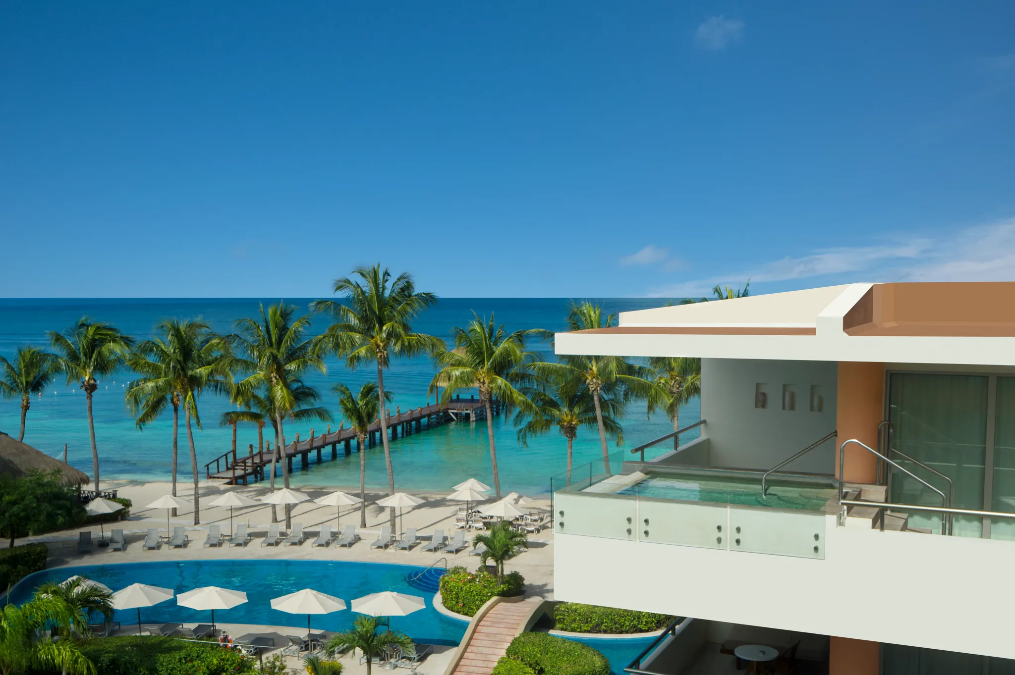 Oceanview pool and rooftop terrace overlooking beach and pier at Secrets Aura Cozumel resort.